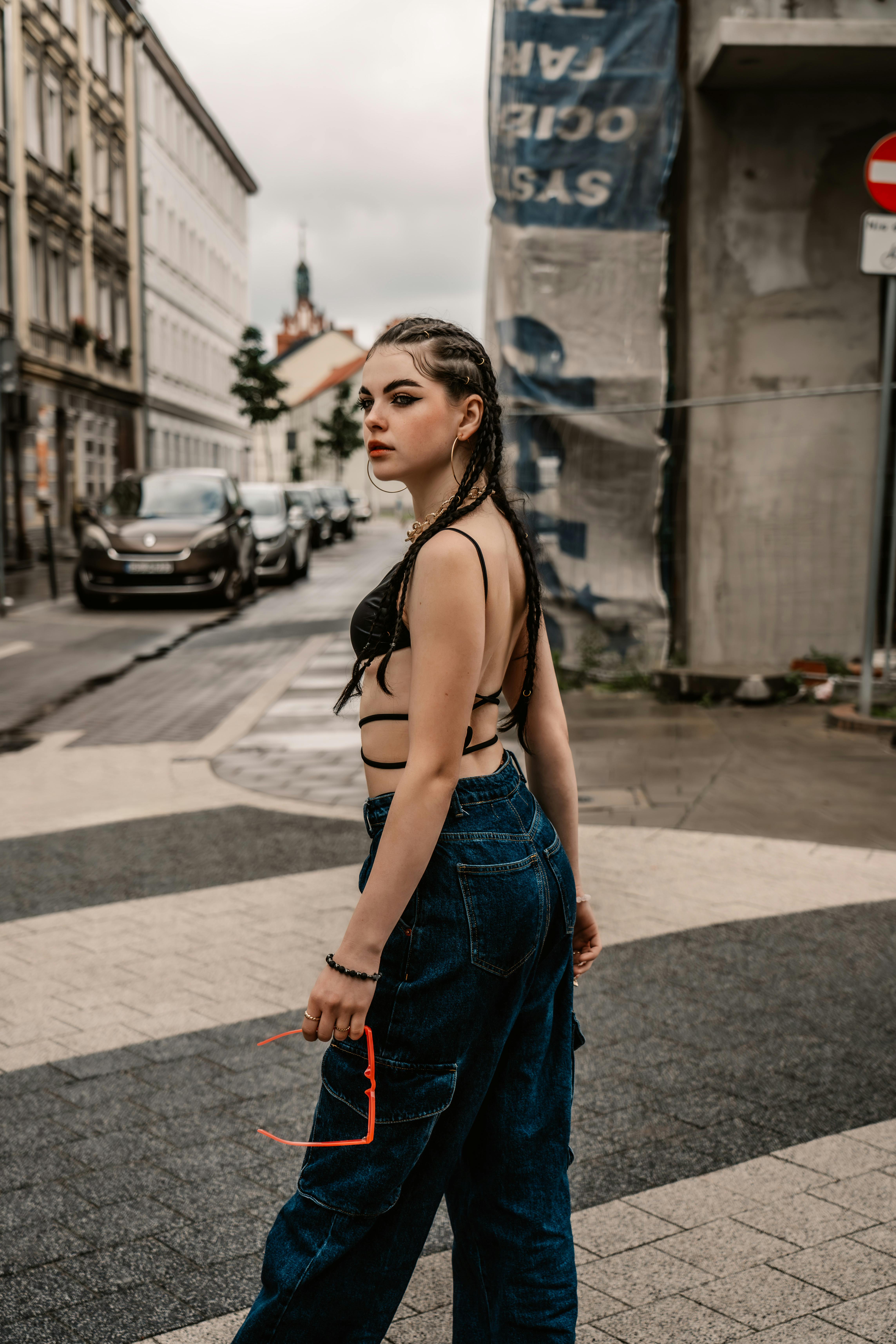 Stylish young woman in denim and bikini top crossing an urban street demonstrating modern city fashion.