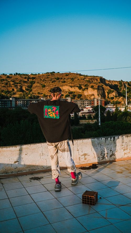 Free A man stands on a rooftop terrace, gazing at a town under the bright blue sky. Stock Photo