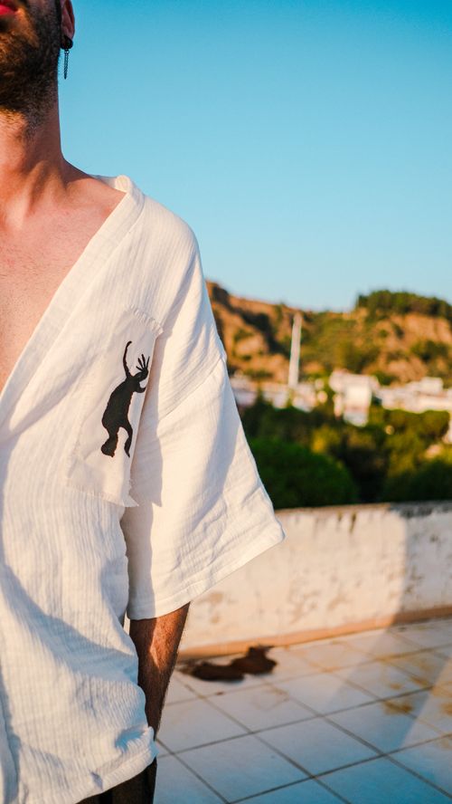 Free A stylish man in a white kimono stands on a sunlit urban rooftop, showcasing modern fashion. Stock Photo