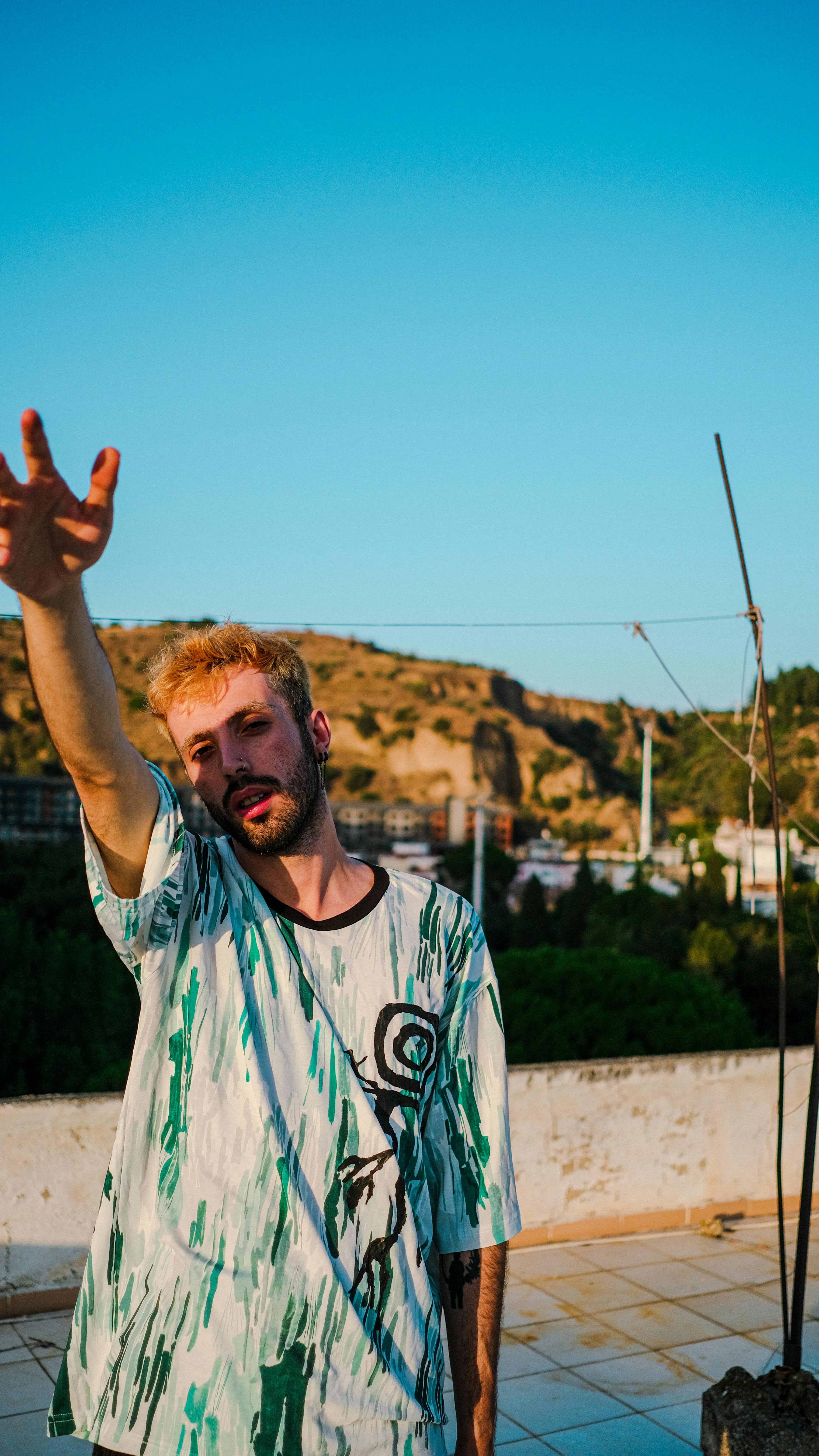 Man with beard and mustache posing outdoors on a rooftop, showcasing fashion in an urban environment.