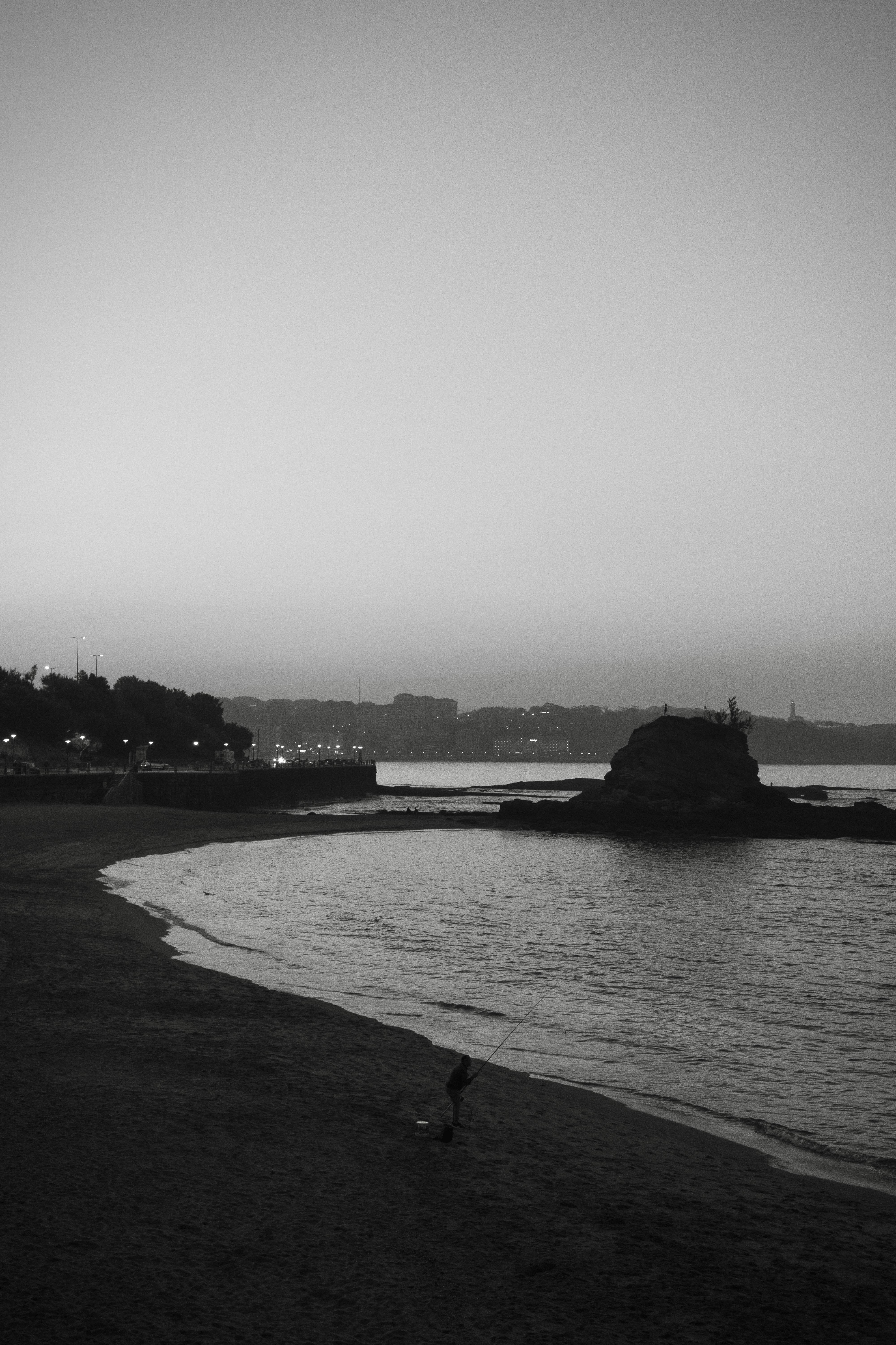 Black and white view of Santander beach at twilight with a lone figure.