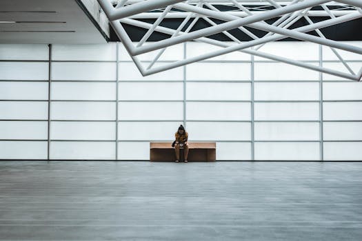 A lone person sits on a bench in a modern, spacious interior with geometric ceiling design.
