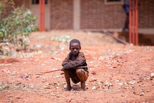 Small Barefoot Boy Holding a Stick in Front of a Building