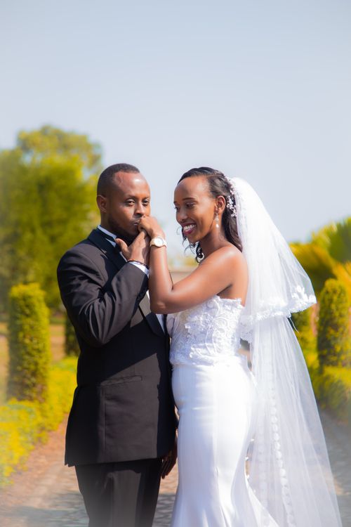 Free Elegant wedding couple posing in a lush garden, bride in white gown and groom in black suit. Stock Photo