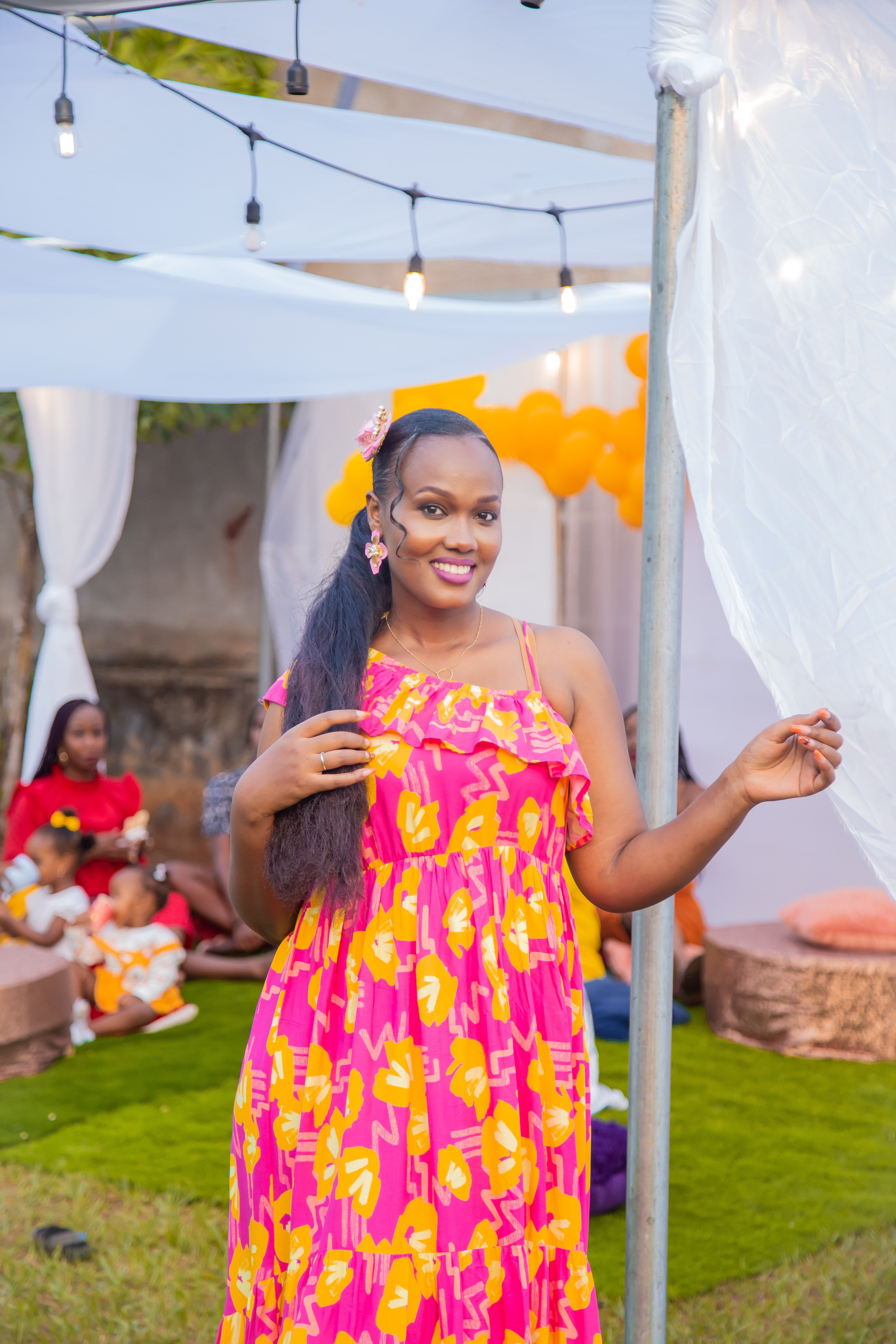 Smiling woman in a vibrant floral maxi dress at an outdoor celebration.