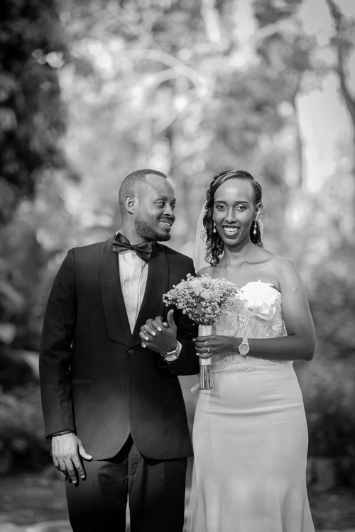 Free Black and white portrait of a smiling newlywed couple outdoors, holding a bouquet. Stock Photo