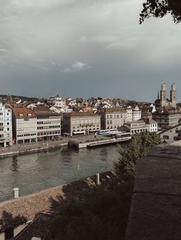Charming view of Zurich's historic old town and Grossmünster along the Limmat River under a cloudy sky.