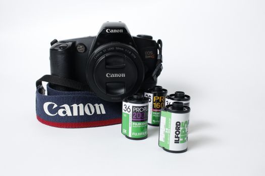 Canon EOS camera with film rolls, showcasing photography equipment on a neutral background.