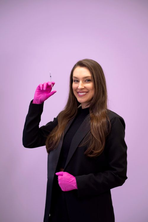 Free Smiling beautician wearing gloves holds syringe against a purple background. Stock Photo