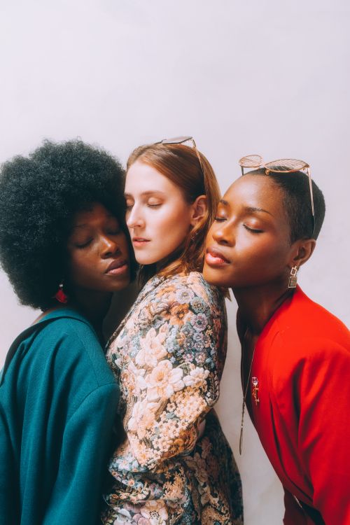 Free Three women of diverse ethnicities embracing with eyes closed, showcasing modern fashion indoors. Stock Photo