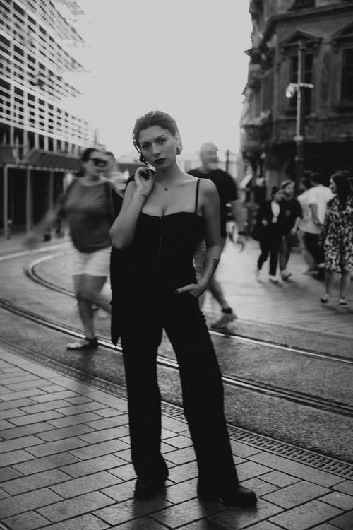 Free A woman in black attire poses confidently on a bustling city street. Stock Photo