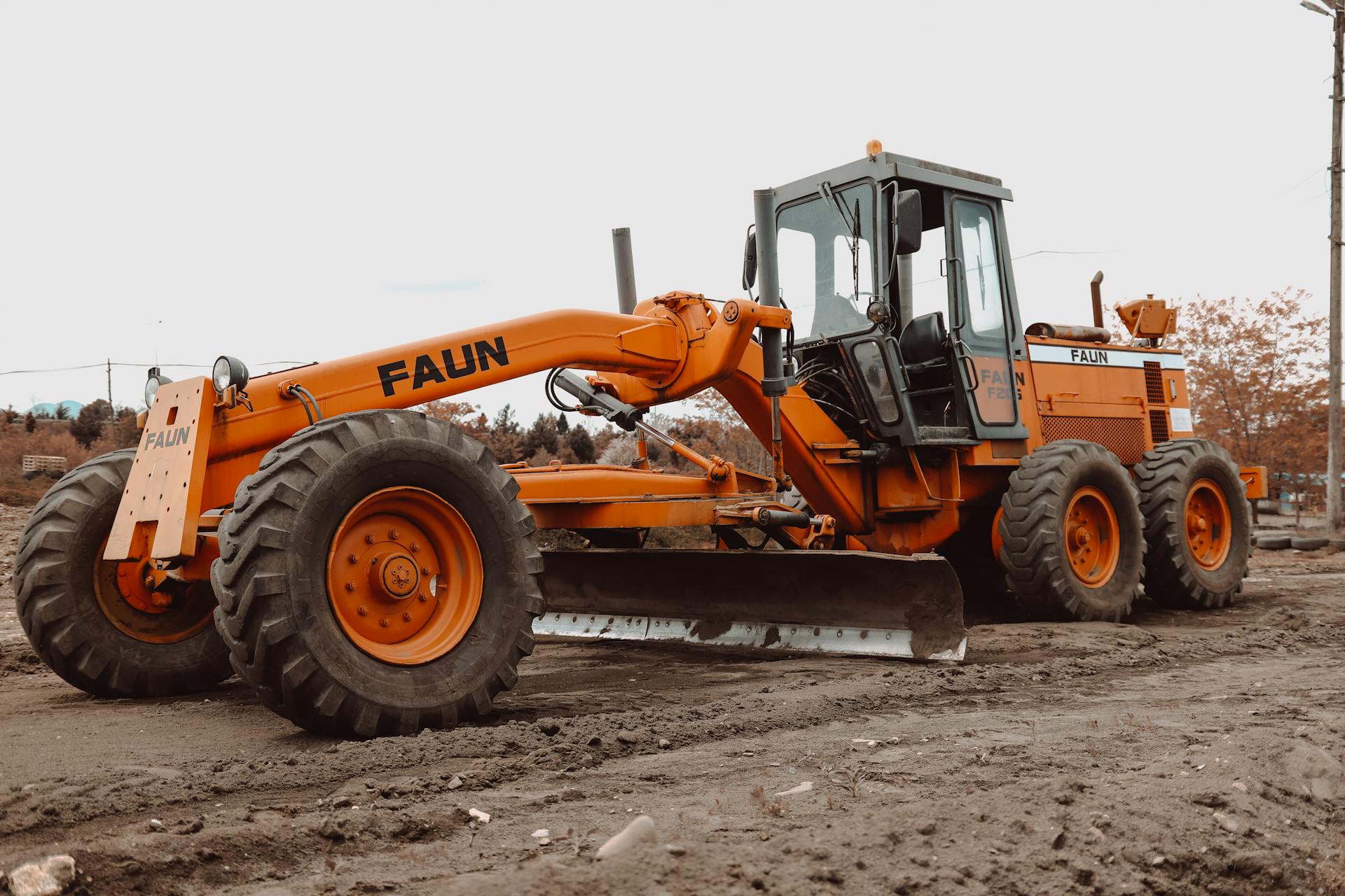 An orange grader vehicle at work on a muddy construction site, showcasing heavy machinery.