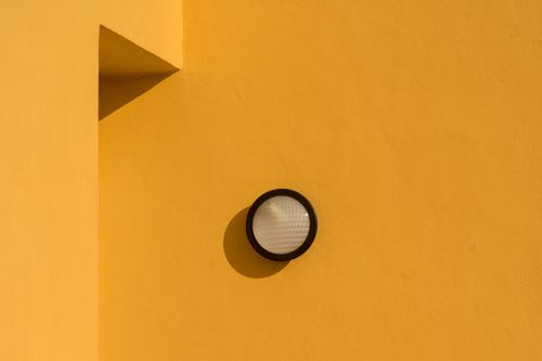 Free A simple and elegant light fixture casting shadows on a yellow wall, capturing minimalism. Stock Photo