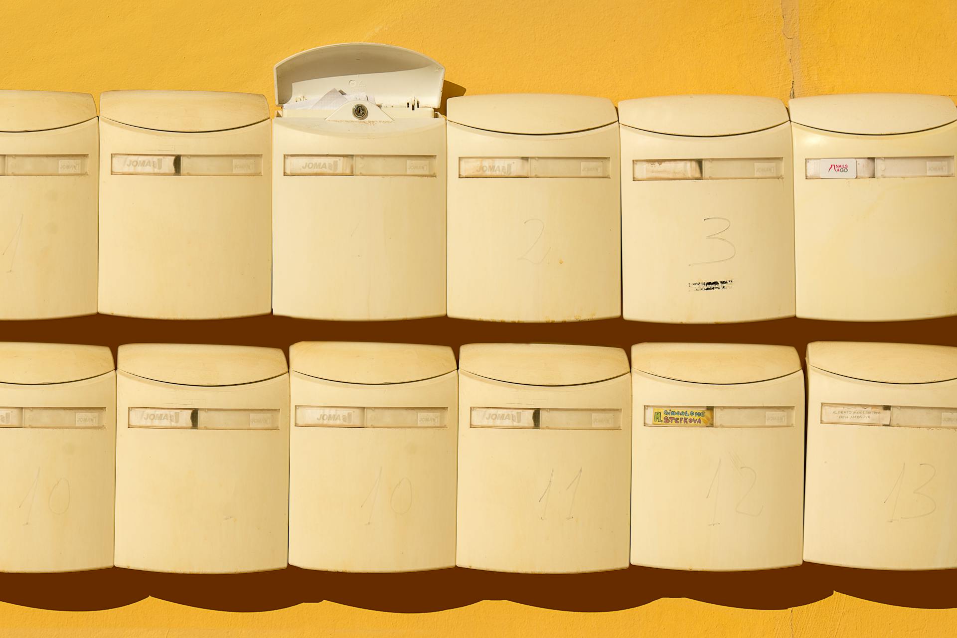 Beige mailboxes mounted on a vibrant yellow wall in a neat arrangement, exuding a modern urban vibe.