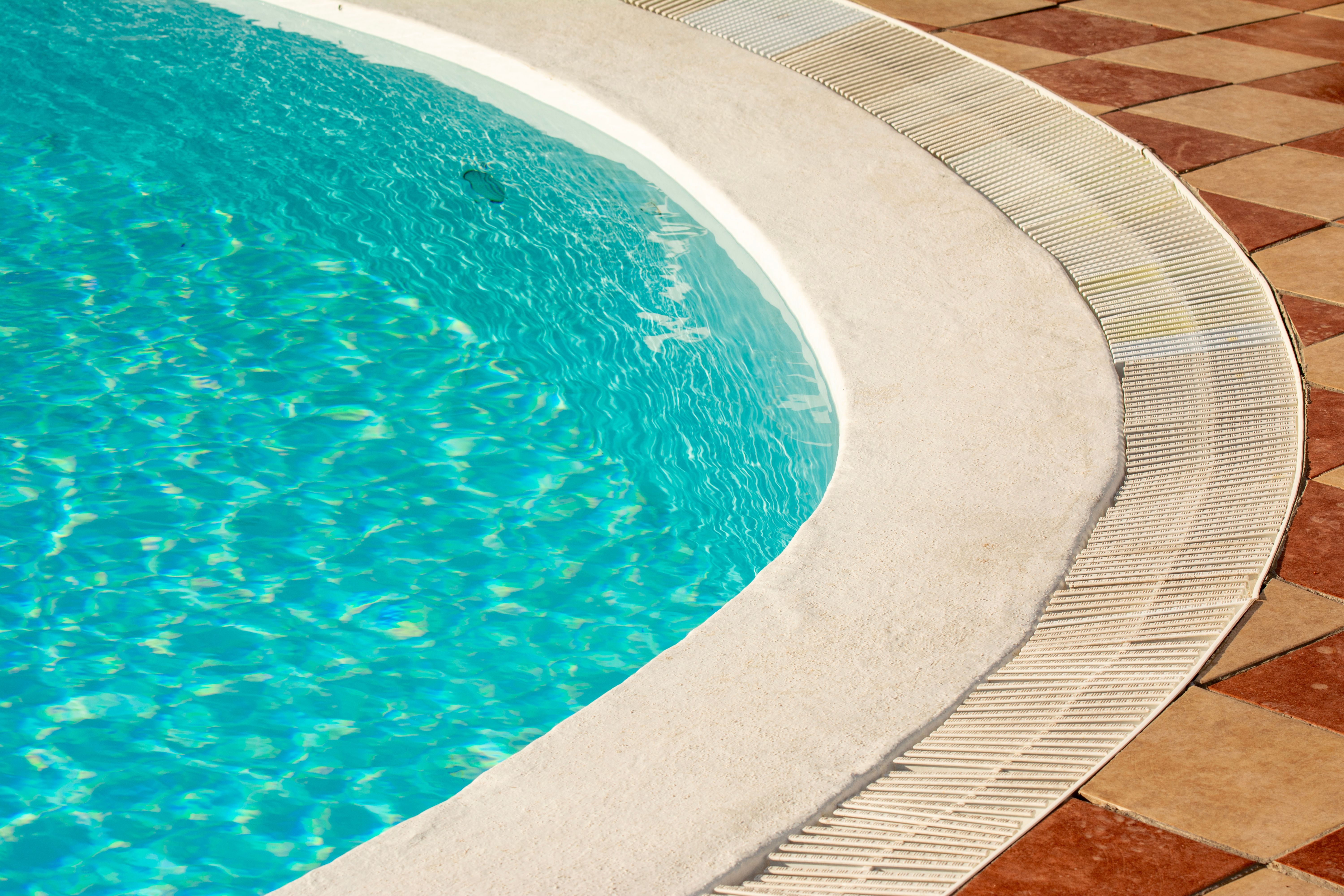 A tranquil sunlit view of a luxurious poolside setting with glistening water and elegant tile work.