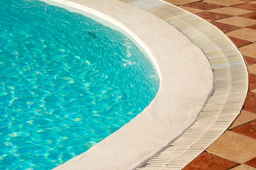 Free A tranquil sunlit view of a luxurious poolside setting with glistening water and elegant tile work. Stock Photo