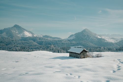 Free Wooden cabin amidst snow-covered mountains under clear sky. Stock Photo
