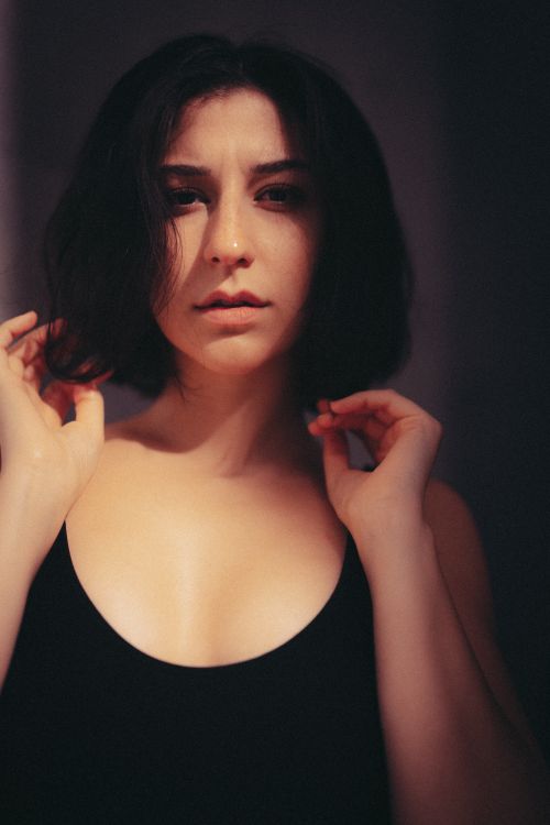 Free Dramatic portrait of a woman in a black tank top, captured in soft light indoors, exuding a moody aesthetic. Stock Photo