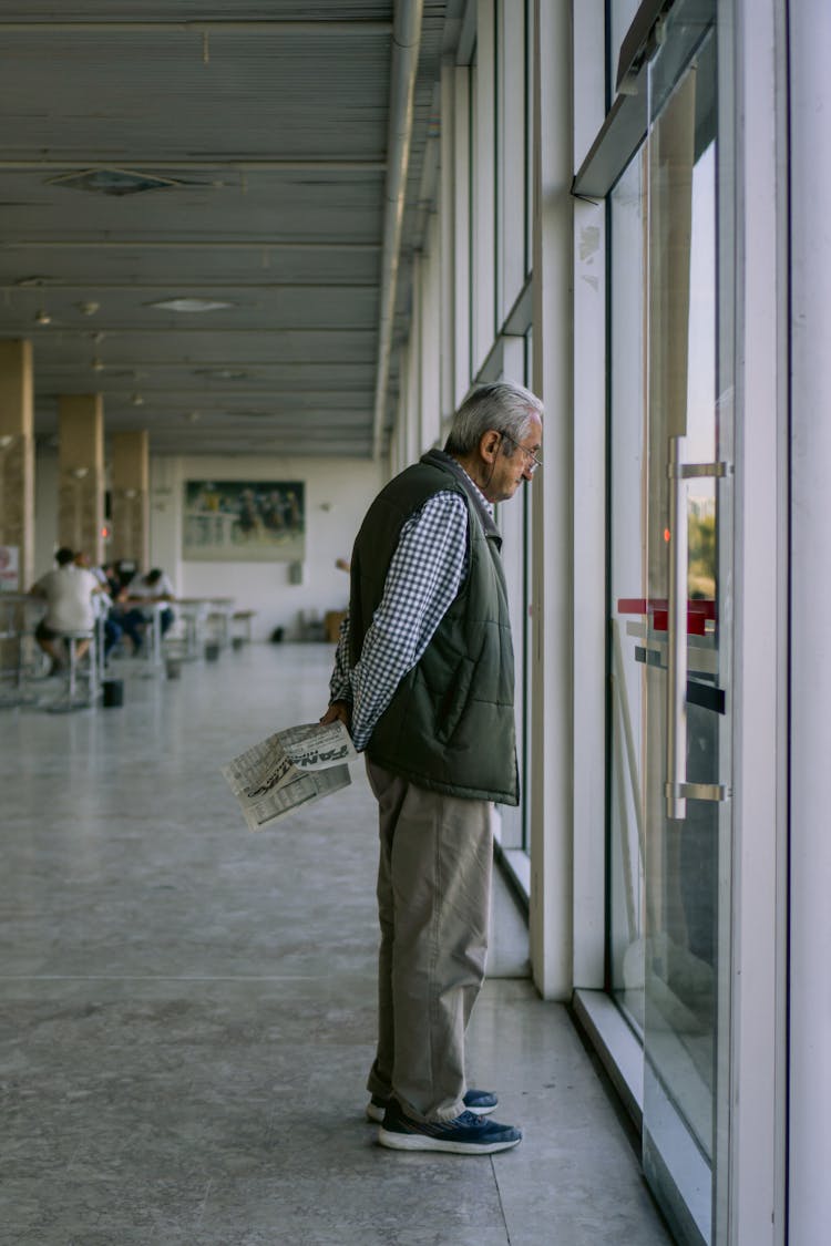 Elderly Man Looking Out Of Window At Airport