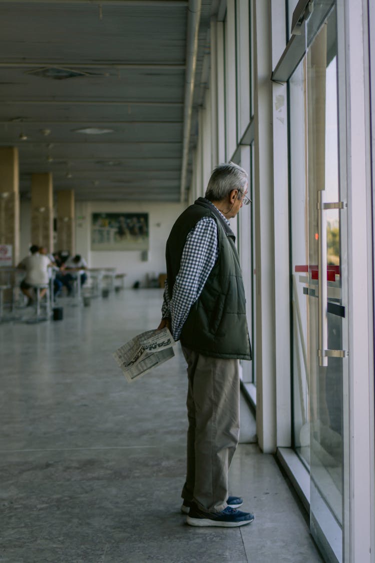 Elderly Man In Shirt Looking Out Of Window At Airport