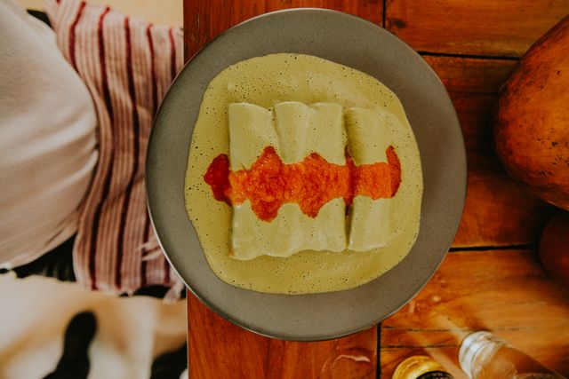 Top-down view of enchiladas with green sauce and red salsa on a rustic wooden table.