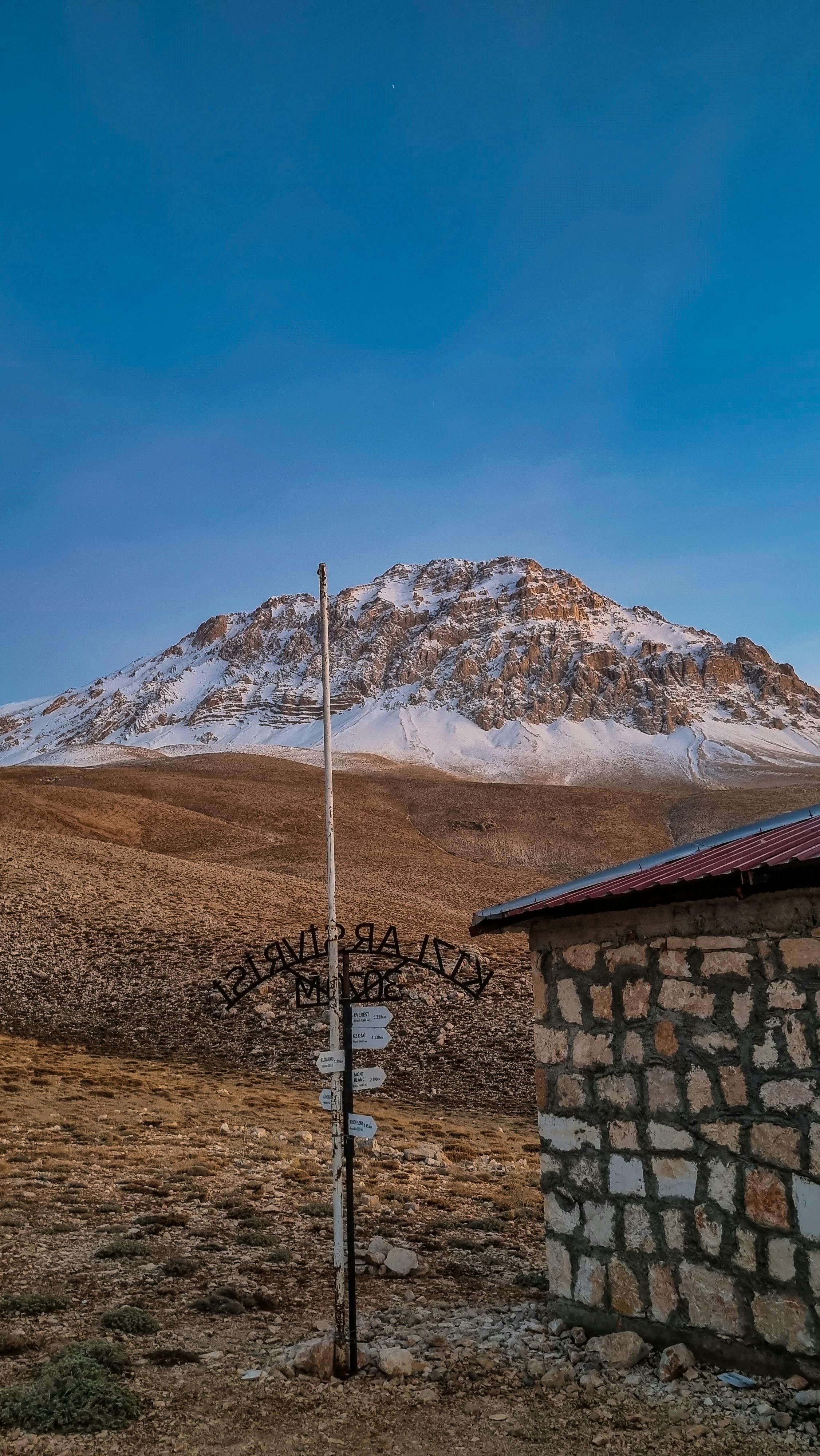 Snow-capped mountain view in Antalya, Turkey with a rustic stone building in the foreground.