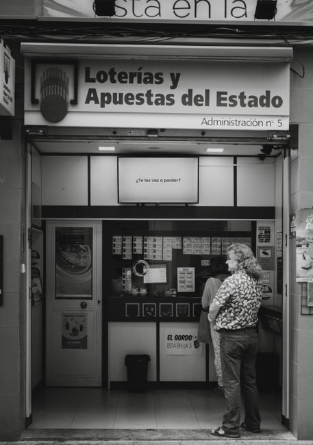 A candid black and white capture of people waiting outside a lottery kiosk.