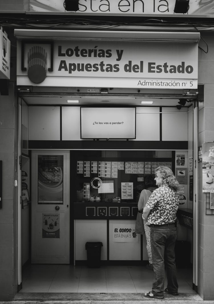 Black And White Photo Of People Waiting In Line At A Lottery Kiosk