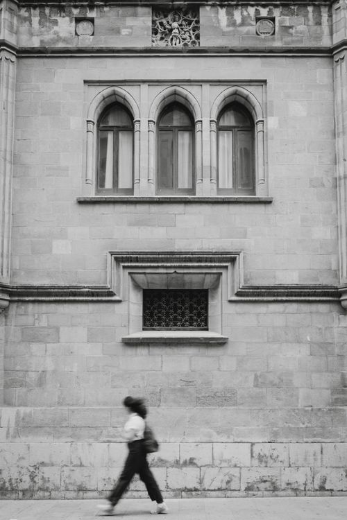 Free Elegant black and white photo of a woman walking past an ornate building facade. Stock Photo