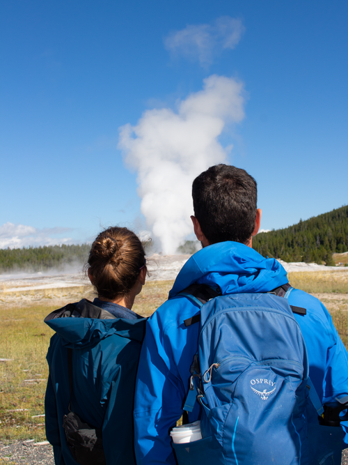 Free A couple watches the Old Faithful geyser erupt at Yellowstone National Park. Stock Photo