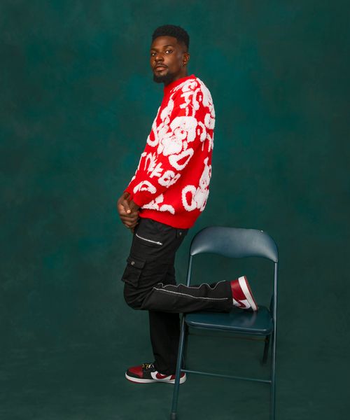 Free A fashionable man posing confidently in a studio, showcasing a vibrant red sweater with artistic patterns. Stock Photo