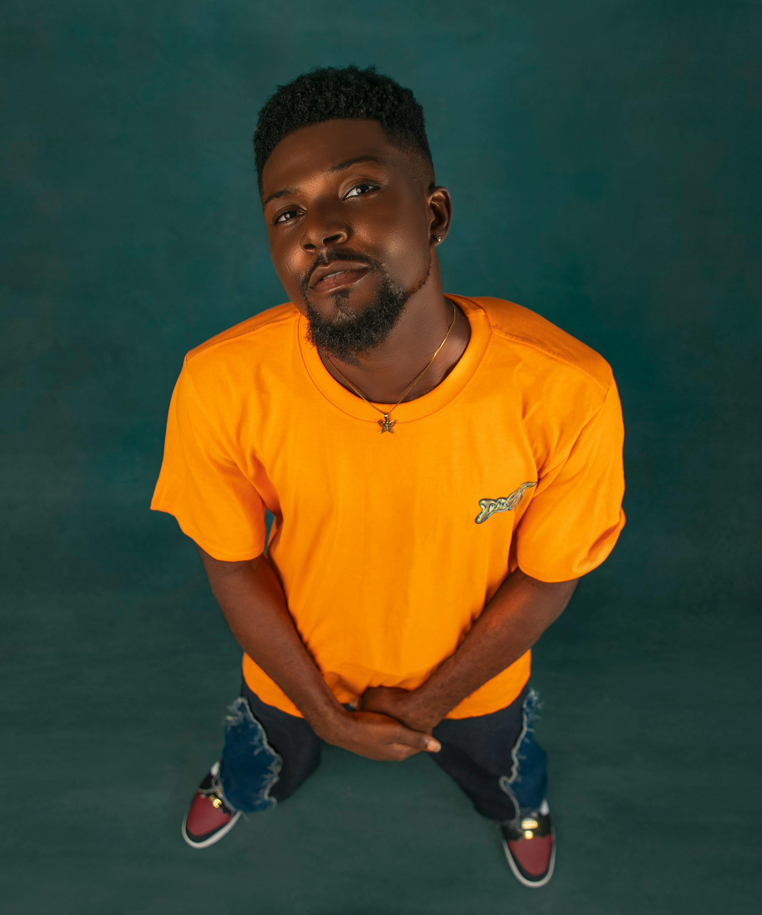 Confident black man in yellow t-shirt looking up at camera with a casual pose.