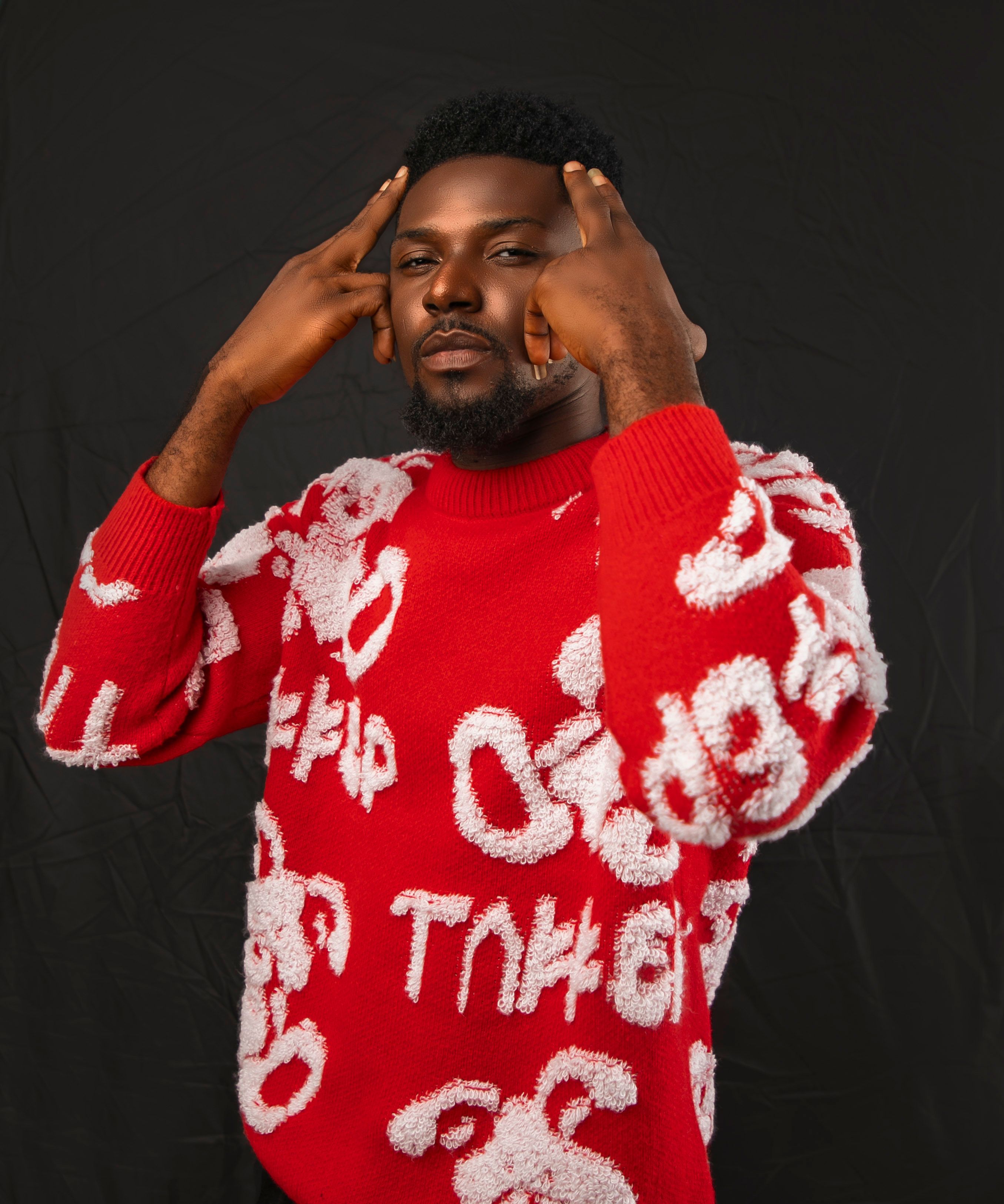 Model wearing a trendy red sweater gestures in a studio photoshoot, showcasing modern fashion style.