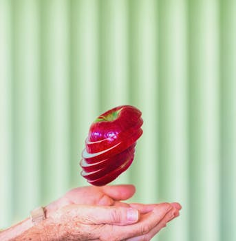 A sliced red apple floating above hands in front of a colorful background.