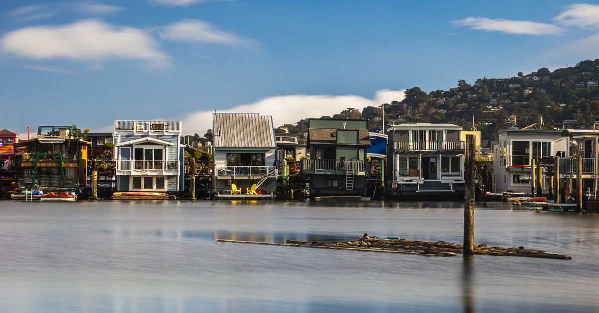 Charming waterfront homes lining a serene river with a backdrop of hills.