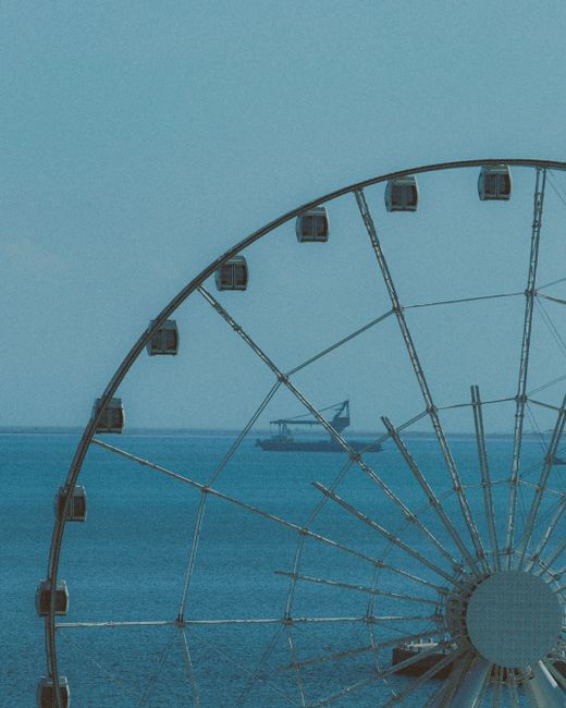 A ferris wheel stands against a serene sea backdrop, evoking a sense of tranquility and adventure.