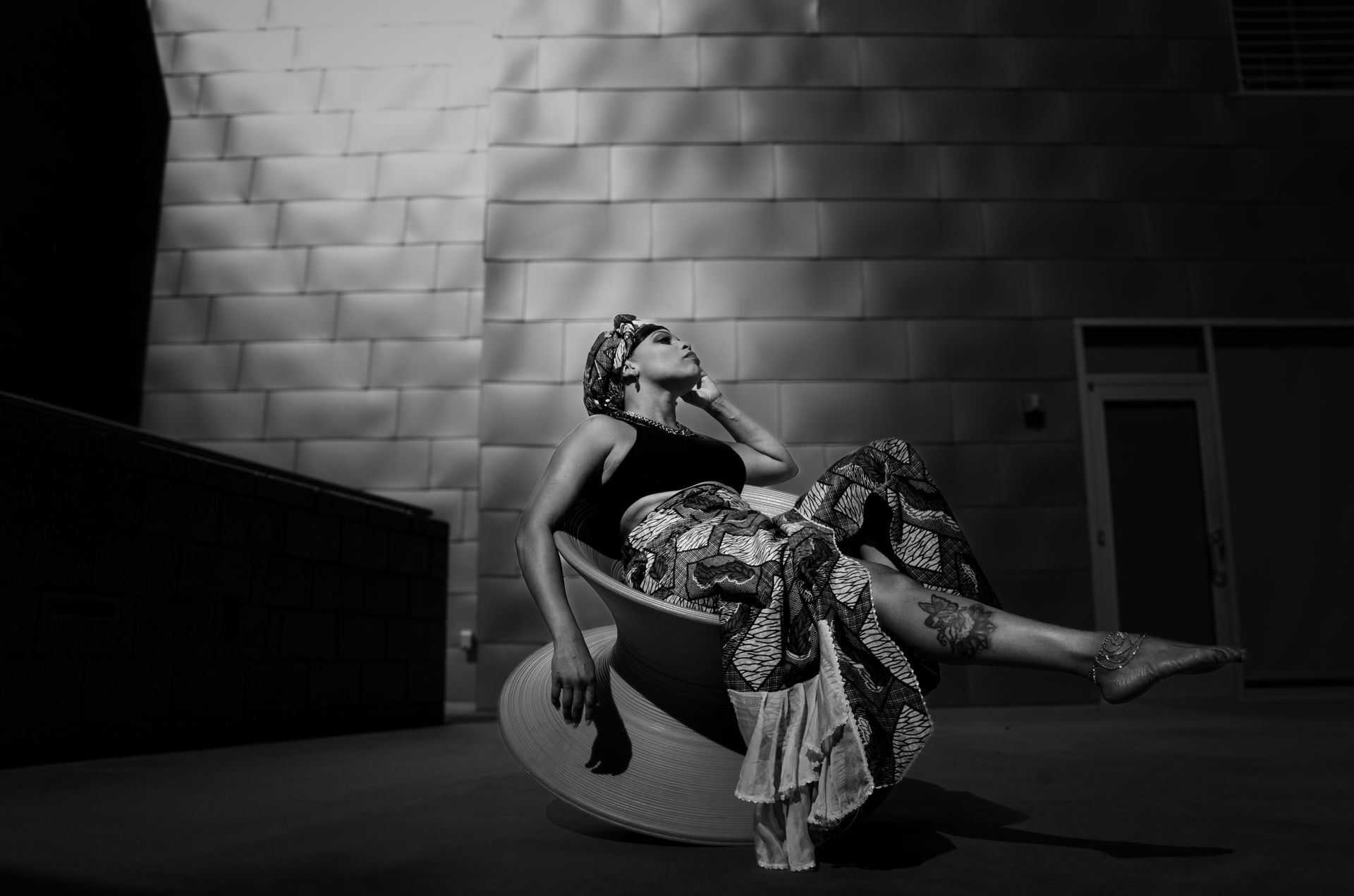 A stylish woman in African maxi skirt and headscarf poses in a modern black and white setting.