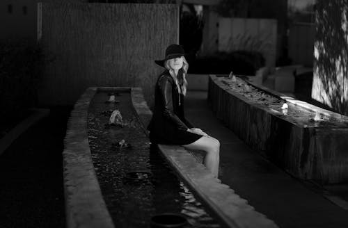 Black and White Photo of a Woman in Elegant Black Hat and Dress Sitting at a Fountain