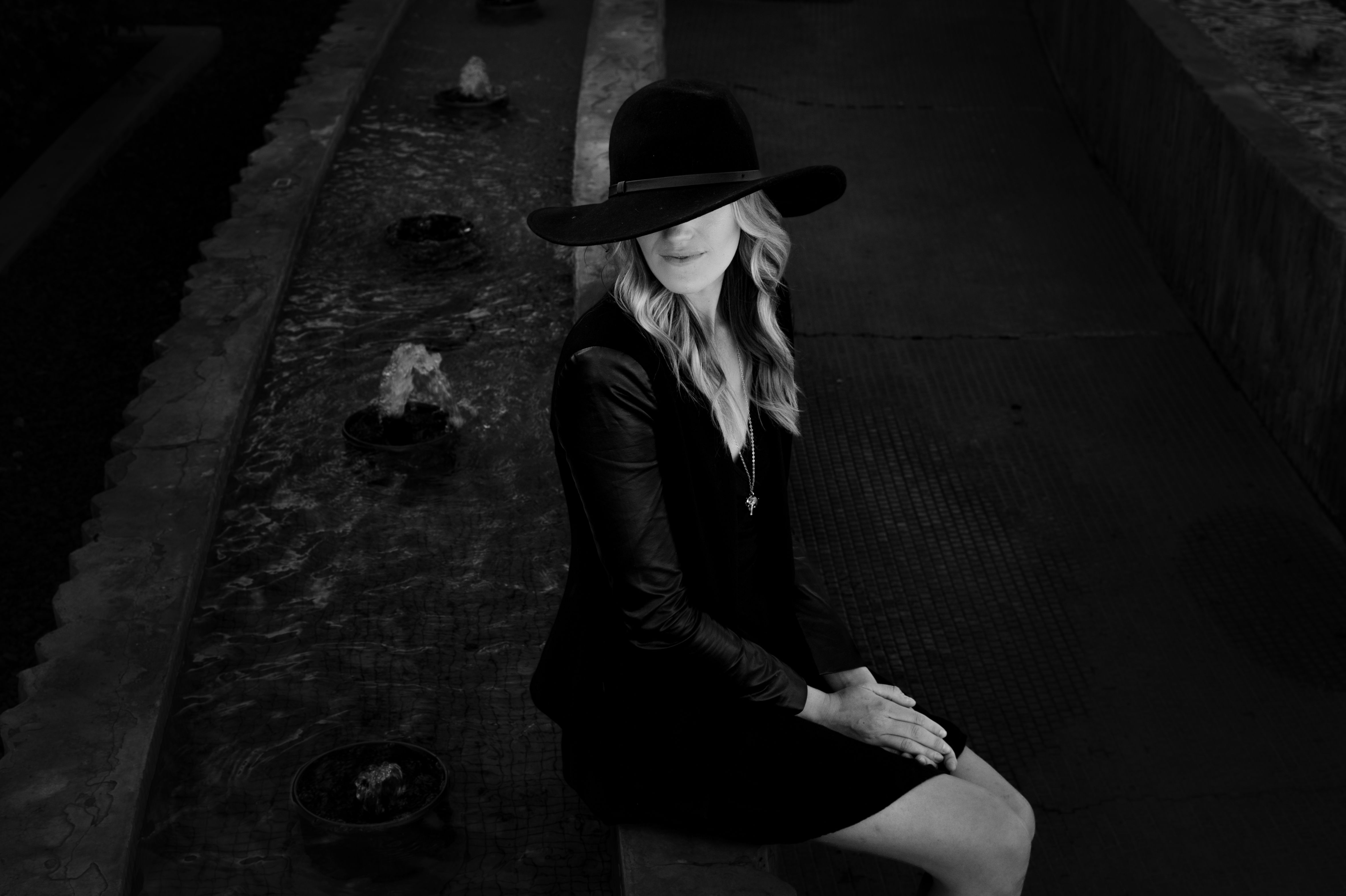 Woman in Elegant Black Wide-Brimmed Hat and Dress Sitting by a Fountain ...