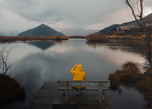 Tourist in a Yellow Raincoat Sitting on Bench by the Lake Wakatipu