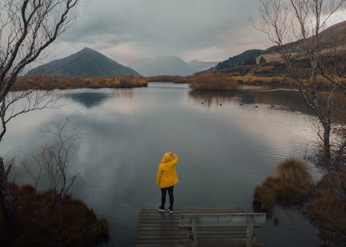 Tourist in a Yellow Raincoat Looking at Birds Swimming in a Mountain Lake