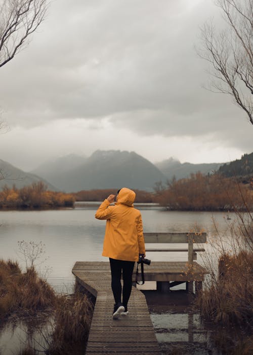 Tourist in a Yellow Raincoat Carrying a Camera at Lake Wakatipu on a Rainy Day