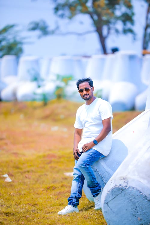 Young Man in a White T-Shirt and Jeans Leaning against a White Bale 