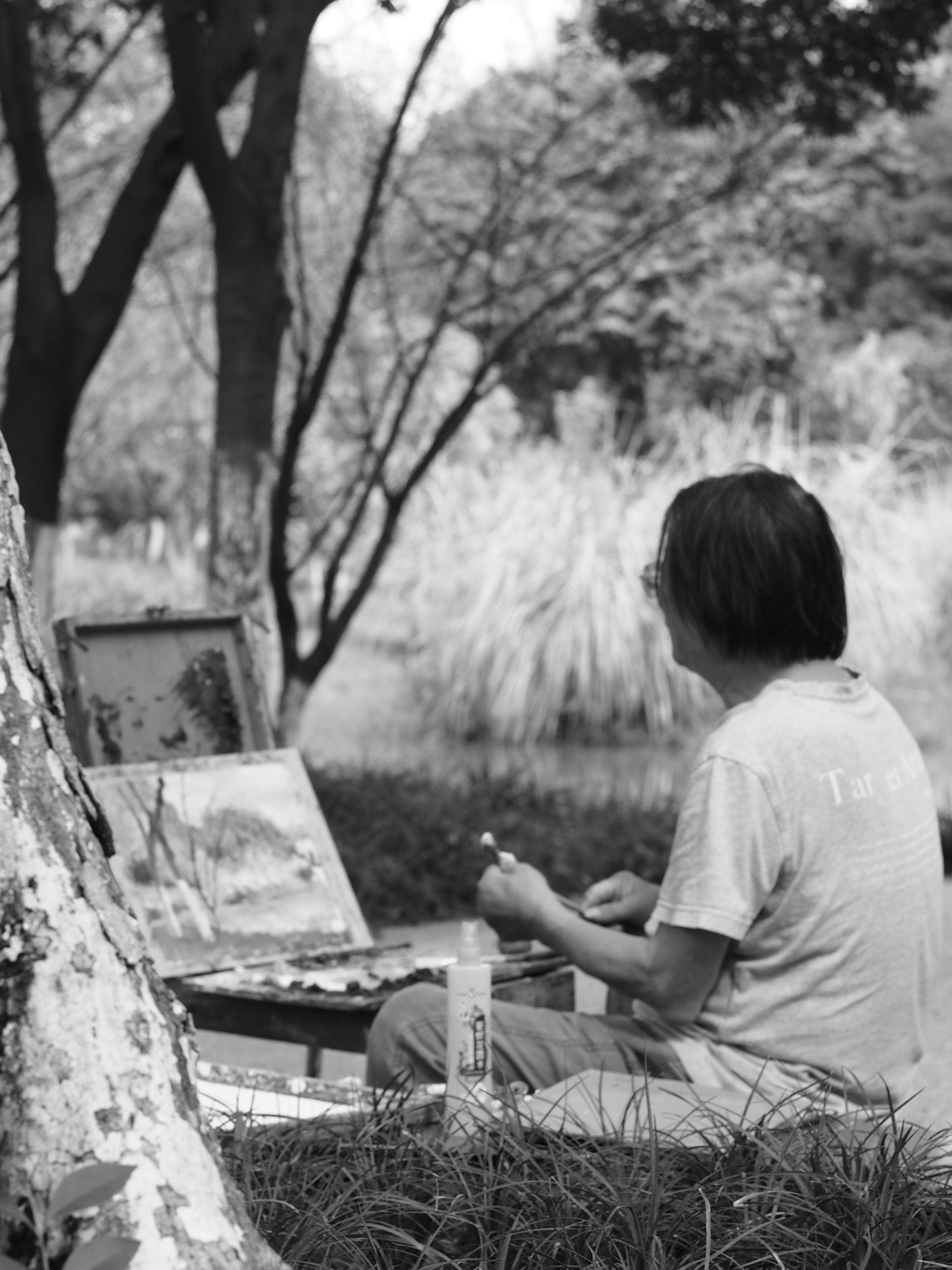 Black and white photo of an artist painting in a serene park setting, capturing creativity and tranquility.