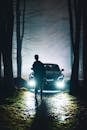 Man with Camera in Front of Car on Forest Path at Night