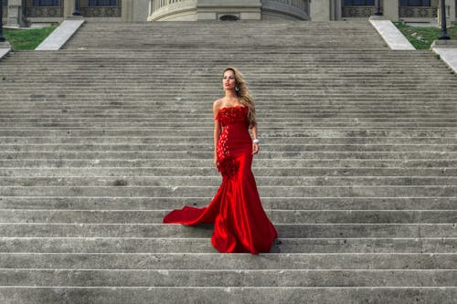 Glamour Model in Red Dress Standing on Stairs