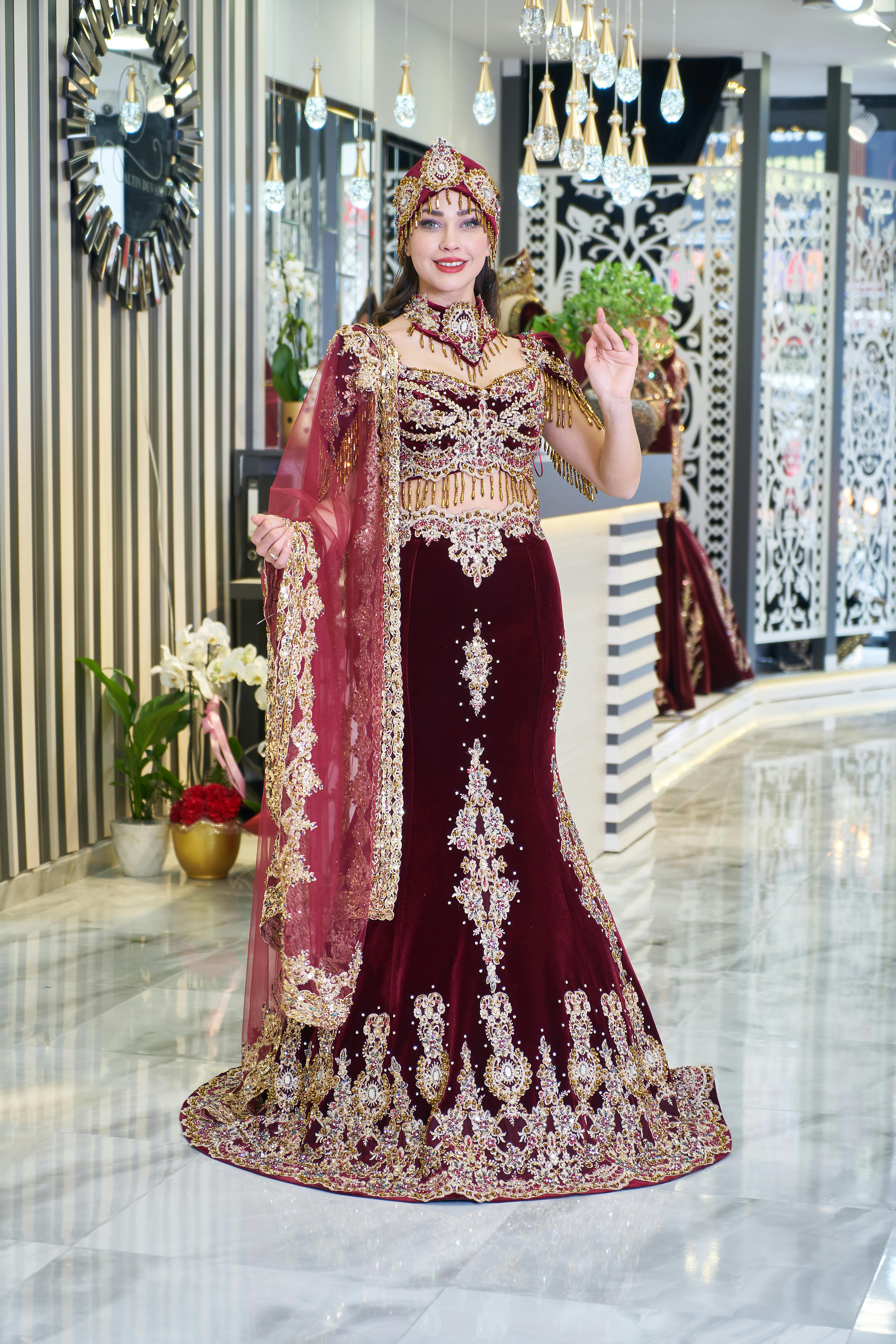 Free A beautiful bride wearing an ornate burgundy and gold traditional caftan indoors. Stock Photo