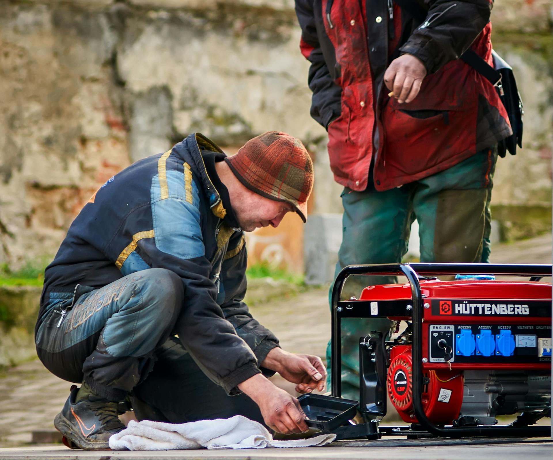 Two technicians working on a red HÜTTENBERG power generator outdoors.