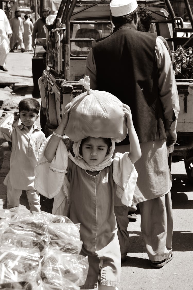 Small Child Carrying A Bag Of Potatoes On Her Head