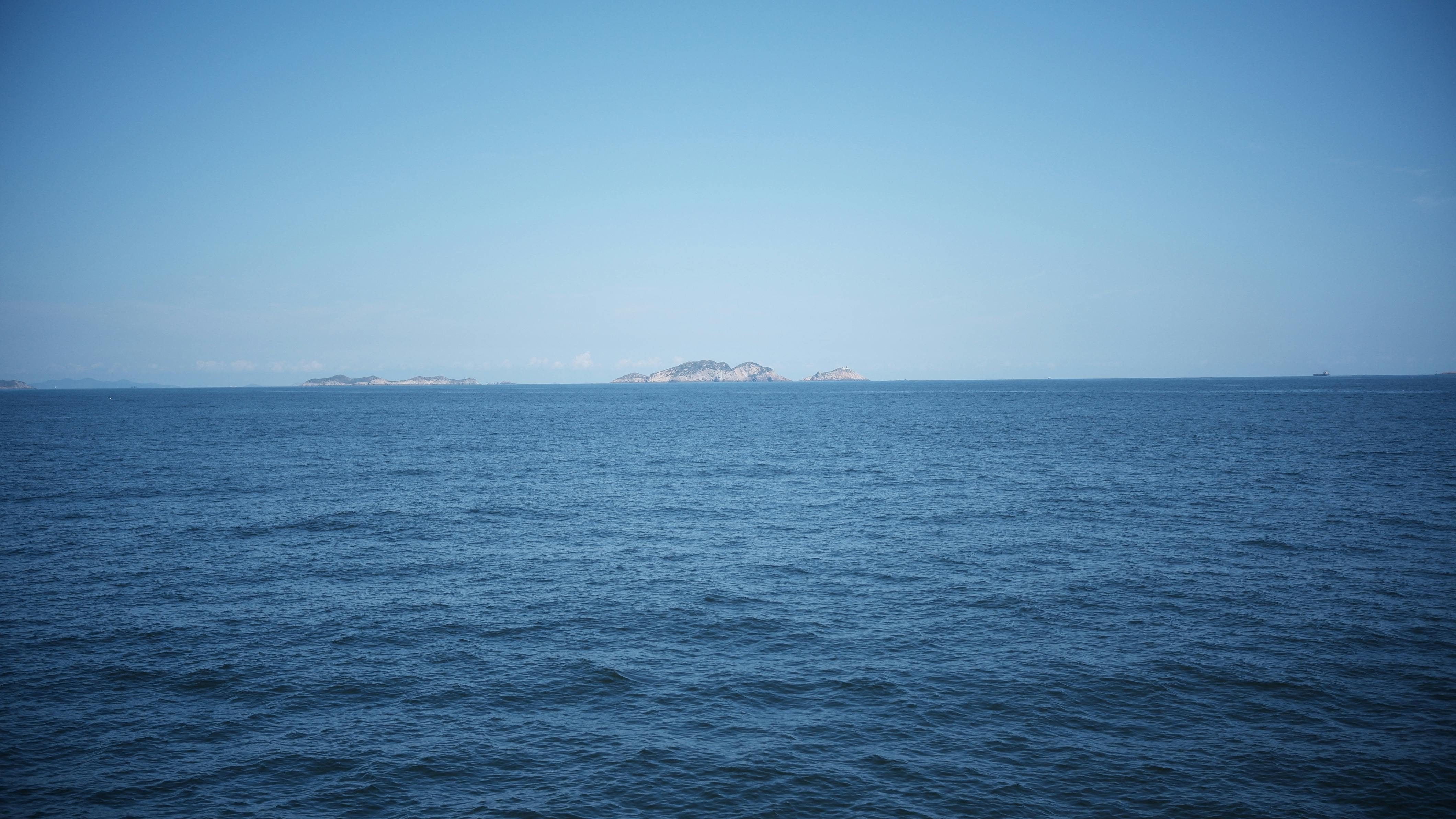 Calm ocean waters meet the horizon with distant islands under a clear blue sky.